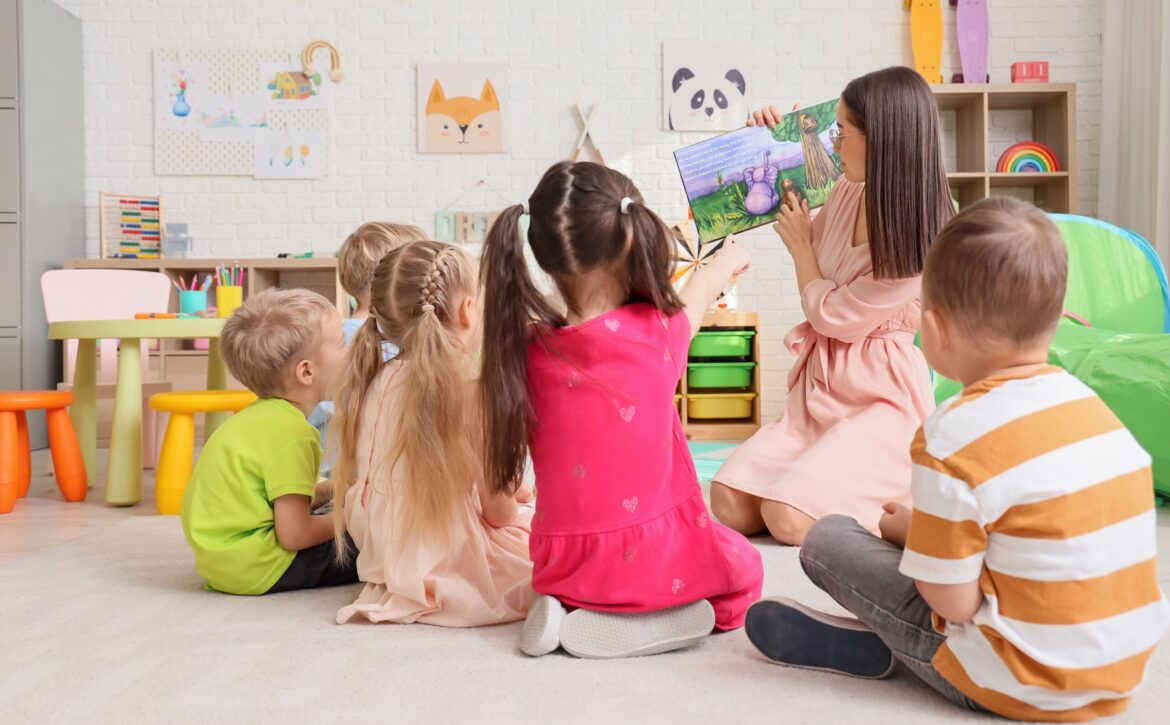 Nursery,Teacher,Reading,Story,To,Little,Children,In,Kindergarten,,Back